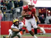  ?? AP PHOTO BY AARON GASH ?? Wisconsin’s Jonathan Taylor runs past Michigan’s Chris Hanlon during an NCAA college football game, Nov. 18, 2017, in Madison, Wis.