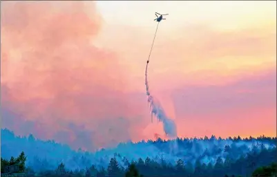  ?? JEFF CHIU / ASSOCIATED PRESS ?? A helicopter drops water on the wildfire-ravaged Oakmont area of Santa Rosa, California, on Thursday. A forecast for gusty winds and dry air threatened to fan the fires, which were fast becoming the deadliest and most destructiv­e in California history....