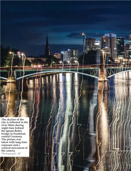  ?? Photograph: AP ?? The skyline of the city is reflected in the river Main during night time behind the Ignatz-Bubis bridge in Frankfurt, central Germany. The picture was taken with long time exposure and a vertical movement of the camera.