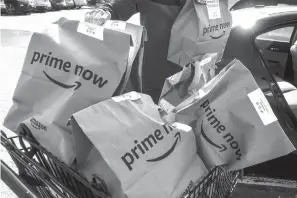  ?? Associated Press ?? Amazon Prime Now bags full of groceries are loaded for delivery by a part-time worker outside a Whole Foods store on Thursday in Cincinnati. Amazon, which owns Whole Foods, plans to roll out two-hour delivery at the organic grocer this year to those...