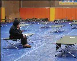  ?? PHOTOS BY JOSIE LEPE ?? Coyote Creek unhoused resident Jerusha Kneib, 41, sits on a cot for the night as she starts to watch a show on her phone after arriving to the Red Cross evacuation shelter at Seven Trees Community Center in San Jose on Jan. 4.