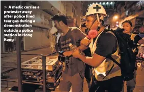  ??  ?? > A medic carries a protester away after police fired tear gas during a demonstrat­ion outside a police station in Hong Kong