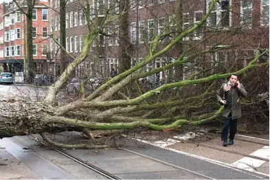  ?? PETER DEJONG/AP ?? ANGIN KENCANG: Seorang lelaki menelepon setelah selamat dari terjangan badai yang mengempask­an motornya di Amsterdam, Belanda. Foto kanan, kereta jaringan Deutsche Bahn berhenti akibat badai di Lamspringe, Jerman.