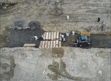  ?? John Minchillo Associated Press ?? WORKERS in protective suits bury bodies in a trench on Hart Island, N.Y. Mass graves were dug on the island in the Bronx, typically a repository of unclaimed dead, as New York became the nation’s pandemic hot spot.