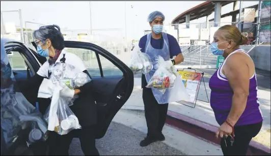  ?? DAMIAN DOVARGANES/AP ?? Los Angeles Unified School District food service workers, Tomoko Cho (far left) and Aldrin Agrabantes help parent Celia Contreras load her free school lunches in to her vehicle on Friday, at the Liechty Middle School in Los Angeles.