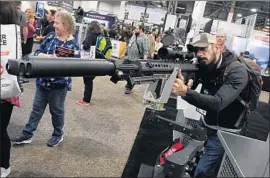  ?? Ethan Miller Getty Images ?? A MAN looks over a .50-caliber Browning machine gun at the Shot Show in Las Vegas. An estimated 65,000 people will attend the four-day event.