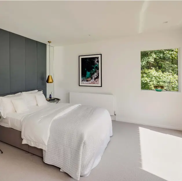  ??  ?? THE MASTER BEDROOM
The blue grey used to create feature walls in the ground floor living space has been continued in the master bedroom (above). The headboard wall panelling was designed and made by the owners, wrapping fabric over wadding on MDF panels.
Full-height mirrors are positioned either side, reflecting the garden at the rear of the room. The gold pendants lights are from Idyll Home.
THE ‘FRAMELESS’ WINDOWS
“We packed out the window reveals to be in line with the window frames, which in turn gives the windows (specified from Velfac) a frameless look — this gives a really clean finish and bespoke look to a standard-sized product,” says Richard.