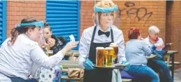  ?? PAUL FAITH / AFP VIA GETTY IMAGES ?? Staff wearing personal protective equipment in the form of face shields and
gloves serve people enjoying a drink in Belfast city centre Friday, as pubs opened their doors after the enforced closure due to the coronaviru­s pandemic.