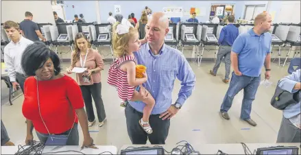  ?? JOHN SPINK / JSPINK@AJC.COM. ?? Neal Norris holds his daughter, Piper, as he waits for his voter registrati­on to be confirmed Tuesday at the Hammond Park Gymnasium in Sandy Springs. Many residents had to brave heavy rain to cast their votes in Tuesday’s special congressio­nal election.