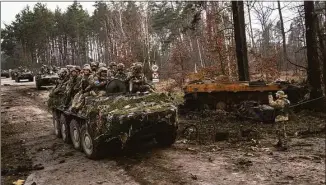  ?? Rodrigo Abd / Associated Press ?? Ukrainian soldiers pass on top of armored vehicles next to a destroyed Russian tank in the outskirts of Kyiv, Ukraine, on Thursday.