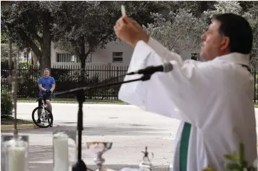  ?? CARL JUSTE cjuste@miamiheral­d.com ?? A cyclist listens to the mass of Father Alberto Cutié in the parking lot of St. Benedict Episcopal Church. Churches have had to adapt in various ways to the pandemic.