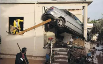  ??  ?? Workers try to remove a car from the entrance of a house in Mandra, on the western outskirts of Athens, Thursday after Wednesday’s flash floods turned streets into torrents of mud and debris that swept away cars, collapsed walls and submerged a section...