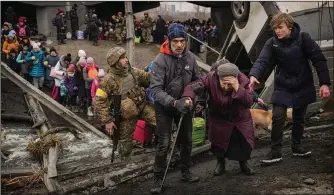  ?? (AP/Vadim Ghirda) ?? An elderly woman is assisted March 5 while crossing the Irpin River on an improvised path under a bridge that was destroyed by Ukrainian troops designed to slow any Russian military advance while fleeing the town of Irpin, Ukraine.