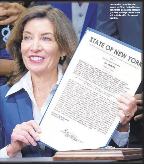  ??  ?? Gov. Hochul shows law she signed on Friday that will reduce the inmate population at Rikers (far left), although the measure will not take effect for several months.