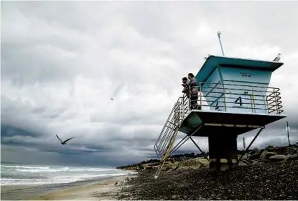  ?? EDUARDO CONTRERAS ?? Abel Salazar (left) and his sister Saray Salazar, who are from Imperial County, watch the stormy sea and sky from their perch at Torrey Pines State Beach on Wednesday. The storm dropped heavy rain and produced flashes of lightning across the region.
U-T