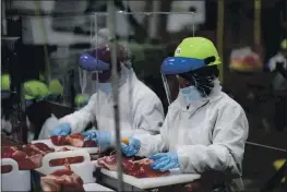  ?? PHOTO COURTESY SMITHFIELD FOODS ?? On May 20, workers inside a Sioux Falls, South Dakota, pork processing plant wear protective gear and are separated by plastic partitions as they carve up meat.