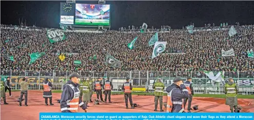  ??  ?? CASABLANCA: Moroccan security forces stand on guard as supporters of Raja Club Athletic chant slogans and wave their flags as they attend a Moroccan Botola football match between Raja and Mouloudia Oujda in Casablanca. — AFP photos