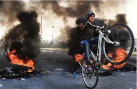  ?? (AFP) ?? A youth drives his bicycle through burning tyres in Karbala, south of Baghdad on Tuesday