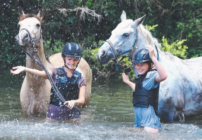  ?? Picture: GLENN HAMPSON ?? Gold Coast Equestrian Centre members Holly Ayres, 14, with Ulysee and Josephine Hermann, 10, with Treasure keep cool at the local creek at Clagiraba.