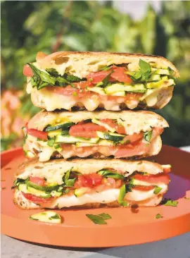  ??  ?? Sliced tomatoes, summer squash, garlic and chives, from top, provide the filling for these tantalizin­g summer sandwiches that resemble panini because they are grilled with melty cheese.