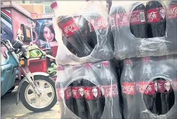  ?? ANDY WONG — THE ASSOCIATED PRESS ?? Bottles of Cherry Coca-Cola with portraits of Warren Buffett are stacked near a dispatch rider’s bike in Beijing. China has promised to retaliate if President Donald Trump escalates the tariff battle.