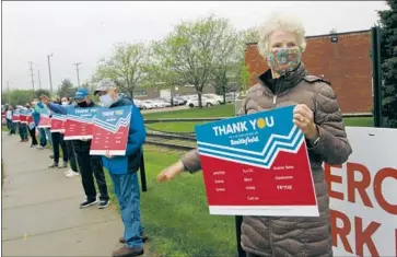  ?? Stephen Groves Associated Press ?? PAT LLOYD of Sioux Falls, S.D., greets workers beginning their shift at a Smithfield pork processing plant. Outbreaks at such plants have shown the difficulty of preventing infections at some businesses.