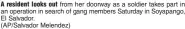  ?? (AP/Salvador Melendez) ?? A resident looks out from her doorway as a soldier takes part in an operation in search of gang members Saturday in Soyapango, El Salvador.