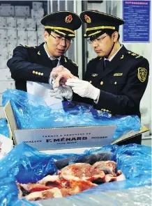  ??  ?? A warehouse worker watches as government inspectors check imported frozen pork in Qingdao in eastern China. A trade war between the United States and China could have serious economic repercussi­ons.