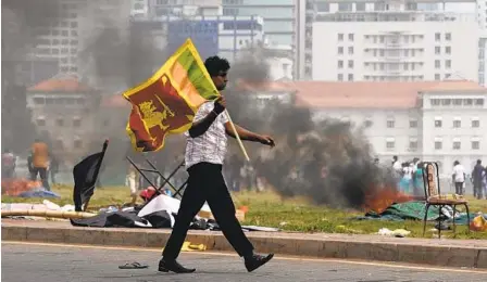  ?? ERANGA JAYAWARDEN­A AP ?? A Sri Lankan government supporter carries a national flag after attacking an anti-government protest outside the official government­al residences in Colombo, Sri Lanka, on Monday. The country has been enduring its worst economic crisis in memory.