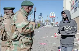  ?? (AFP) ?? South African soldiers interrogat­e a pedestrian in front of a looted mall, in Soweto on Tuesday
