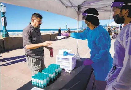  ?? NELVIN C. CEPEDA U-T ?? Dakota Paige (center) and Cameron Mccalliste­r pass out a free mask at Mission Beach on Saturday. They are part of SOS YES, a nonprofit offering free COVID testing.