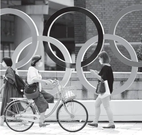  ?? AP ?? In this July 15, 2021 photo, people walk by the Olympic rings installed by the Nippon Bashi bridge in Tokyo.