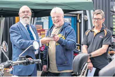  ??  ?? Norman Hyde (left) presents the trike’s key to Simon Weston watched by Trike Design’s Hank Hancock (right). [Photo by Tony Smith]