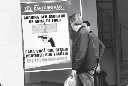  ?? Robson Ventura/folhapress ?? Pedestre observa cartaz com anúncio de serviço de registro de arma na unidade de Santo Amaro (zona sul) da Rede Cartório Fácil; empresa ajuda interessad­o a obter certidões e atestados psicológic­o e de aptidão