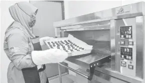  ?? — Gamabr Bernama ?? PORSES BAKAR: Tenaga pengajar program Genius Remaja Fatimah Jusoh memasukkan adunan biskut untuk dibakar ke dalam ketuhar.