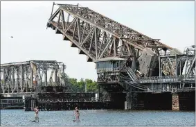  ?? DANA JENSEN/THE DAY ?? Paddle boarders travel down the Connecticu­t River while the railroad bridge between Old Lyme and Old Saybrook rises for boat traffic in the background on Tuesday.