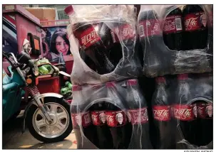  ?? AP/ANDY WONG ?? Bottles of Coke featuring images of Berkshire Hathaway Chairman and CEO Warren Buffett sit near a dispatch rider’s bike Tuesday in Beijing. China is delaying license applicatio­ns from some American companies until progress is made in negotiatio­ns with U.S. trade officials, a business group said Tuesday.