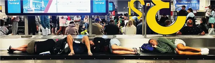  ?? ?? We’re fit to drop: Exhausted holidaymak­ers lay on a carousel at Gatwick as they wait for their bags to arrive in further chaotic scenes at the airport yesterday
