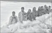  ??  ?? Devotees offers prayers to the rising sun as toxic foam floats on the surface of polluted Yamuna river.