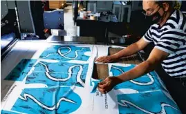  ?? JOSE M. OSORIO/CHICAGO TRIBUNE ?? Francisco Medina monitors a laser cutter making marching band uniform jackets Thursday at R&S Marching Arts in Chicago. Best known as the maker of the Chicago flag mask worn by Mayor Lori Lightfoot, the company is back to making marching band uniforms and flags after pivoting early in the pandemic to 100% mask production.