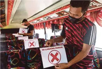  ?? PIC BY GHAZALI KORI ?? Tour bus operator Mohd Nazir Mubin Ibrahim (right) placing a physical distancing sign in his company’s bus in Kuala Terengganu yesterday.