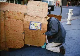  ?? Lea Suzuki / The Chronicle ?? Iuchi Kojiro, who is homeless, retrieves a bag of binders and notes from a cardboard shelter on Powell and O’Farrell streets in San Francisco.