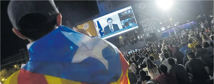  ?? AFP ?? Por TV. El presidente del Gobierno español, Mariano Rajoy, habla ayer al país y rechaza la validez del referéndum catalán. Independen­tistas lo miran en una plaza de Barcelona.