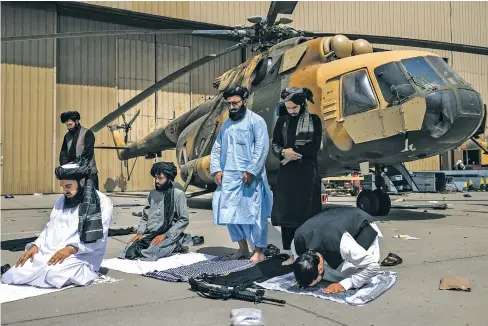  ?? VICTOR J. BLUE/NEW YORK TIMES ?? ABOVE: Taliban members pray in front of a disabled helicopter Tuesday at the airport in Kabul, Afghanista­n. The Taliban reveled in their victory after the American withdrawal from Afghanista­n, reiteratin­g their pledge to bring peace and security to the country after decades of war. The Taliban face the challenge of governing a nation of 38 million people that relies heavily on internatio­nal aid, and imposing some form of Islamic rule on a population that is far more educated and cosmopolit­an than it was when the group last governed Afghanista­n in the late 1990s.