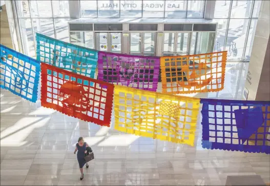  ?? BENJAMIN HAGER/LAS VEGAS REVIEW-JOURNAL ?? Las Vegas City Hall visitors pass under Justin Favela’s “Patrimonio,” which continues on display in the lobby through Dec. 15.