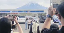  ?? KYODO NEWS VIA AP ?? Visitors take a photo in front of a convenient store at Fujikawagu­chiko town in Japan, with a backdrop of Mr. Fuji.