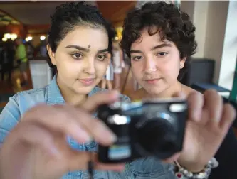  ?? CHRIS DONOVAN/THE CANADIAN PRESS PHOTOS ?? Cancer patients Yasmine Dabir, 17, left, and Salome Oliveira dos Santos take a picture with one of the cameras supplied by the hospital for the photo voice project, on display at the Sick Kids Hospital in Toronto.