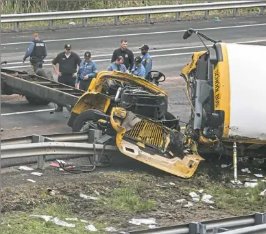  ?? Bryan Anselm/The New York Times ?? Police and paramedics look at what’s left of a school bus after it collided with a dump truck Thursday on Interstate 80 near Mount Olive, N.J. A student and a teacher were killed and dozens of others were injured, officials said.