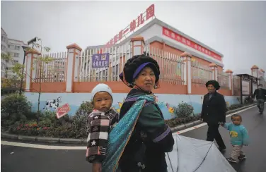  ?? Andy Wong / Associated Press ?? Ethnic minority Chinese walk with kids under a banner reading “I'm a China doll, can speak Mandarin.”