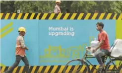  ??  ?? MUMBAI: Indian workers walk past fencing at a constructi­on site for the forthcomin­g metro train project yesterday. — AFP